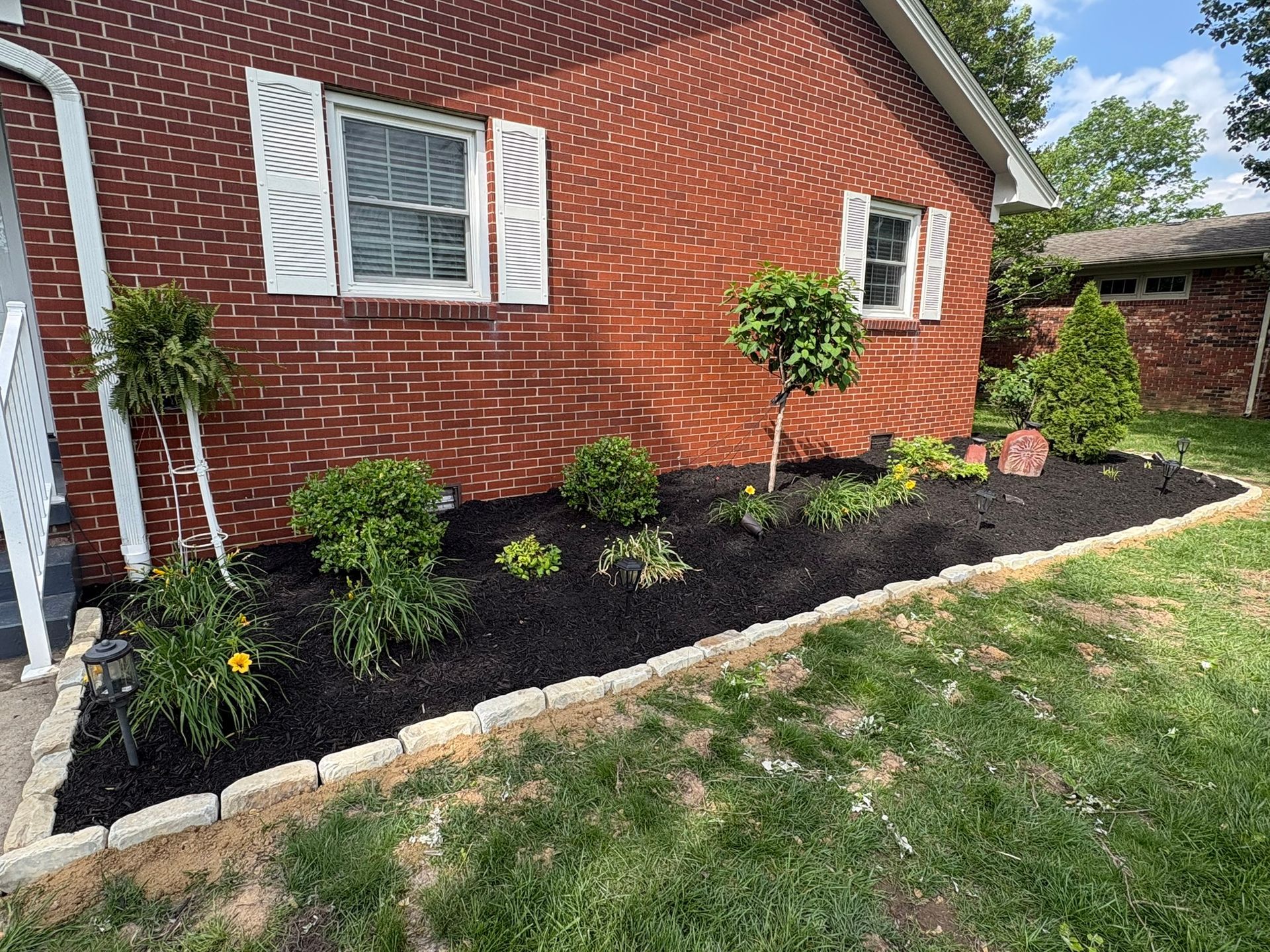 Brick house side yard with fresh black mulch, small shrubs, and a stone border along the lawn