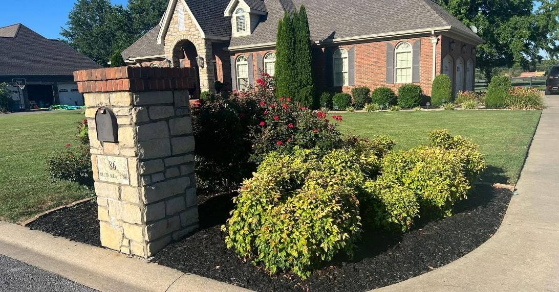 Suburban house with landscaped front yard, stone mailbox, and trimmed shrubs by the curb.