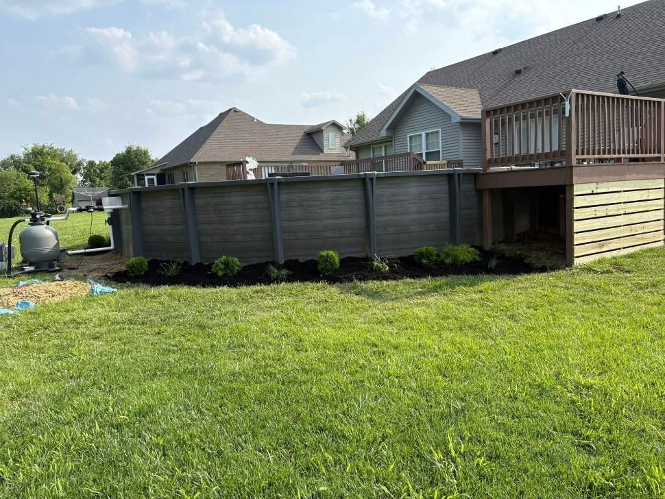 Backyard with green lawn, wooden privacy fence, deck, and neighboring houses under a sunny sky