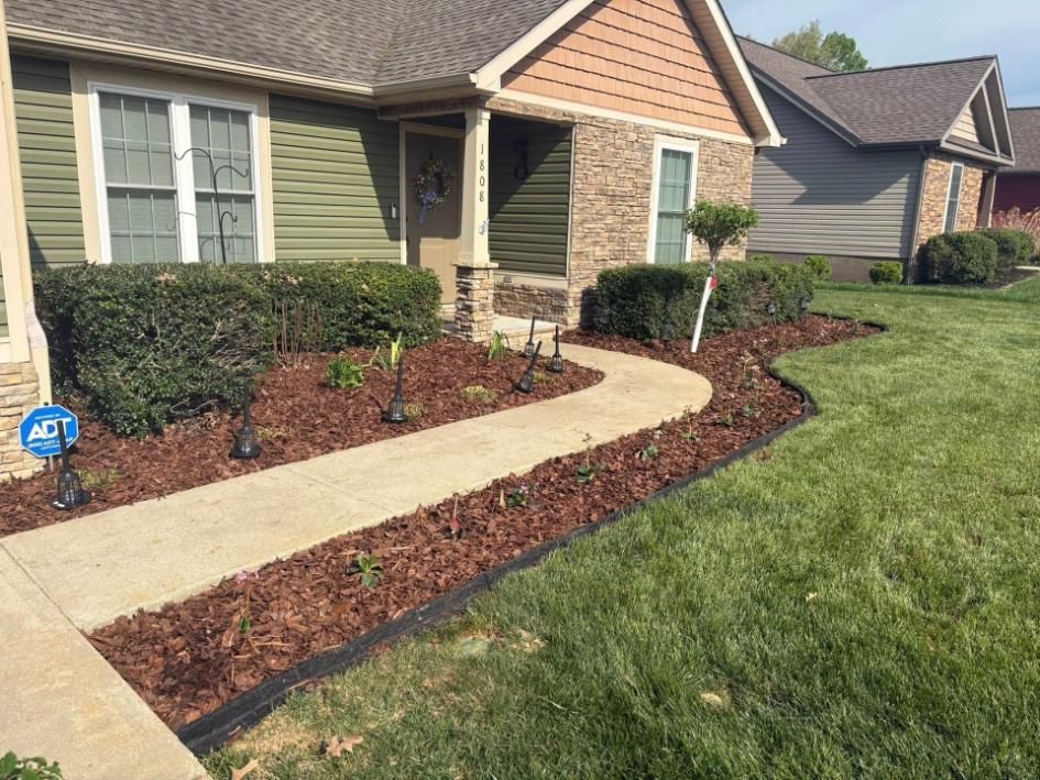 Front yard walkway to a brick house with trimmed shrubs, mulch beds, and green lawn