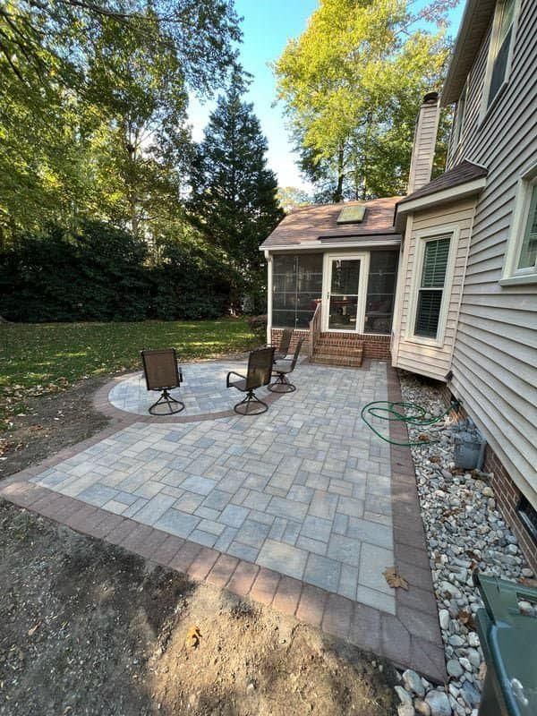 Patio with paver stones, two chairs, and a small brick porch beside a house and trees
