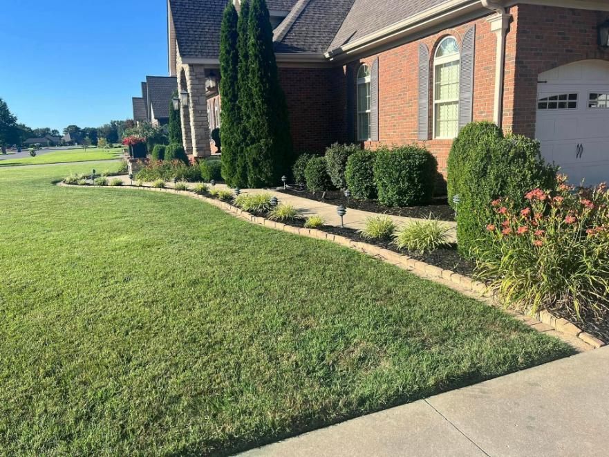 Brick house with manicured lawn, shrubs, and a concrete driveway in bright sunlight