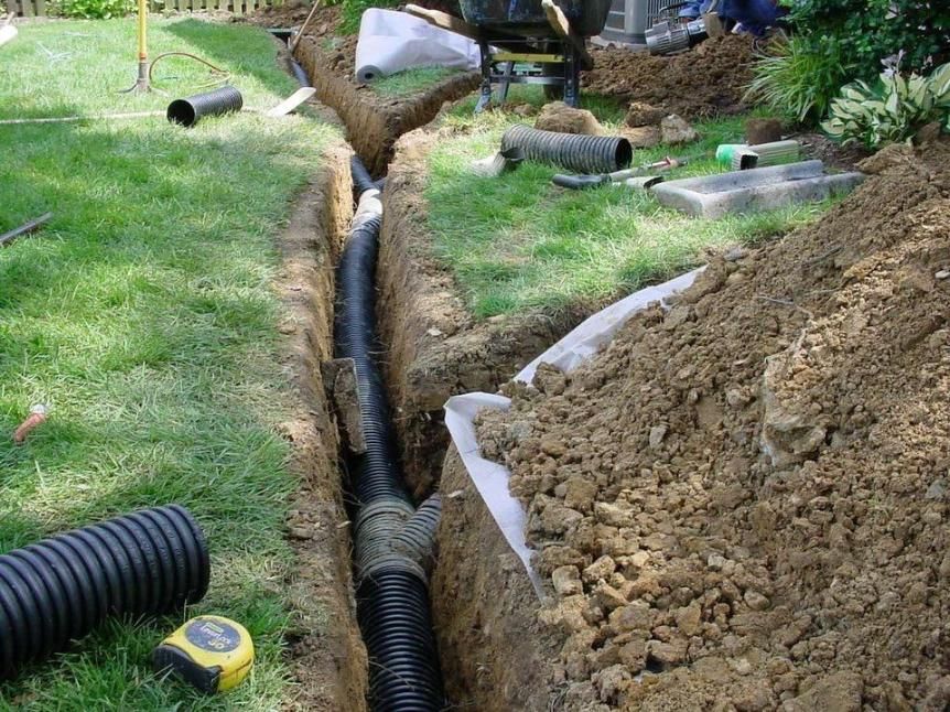 Trenches dug in a grassy yard with black drain pipes and piles of dirt for landscaping work