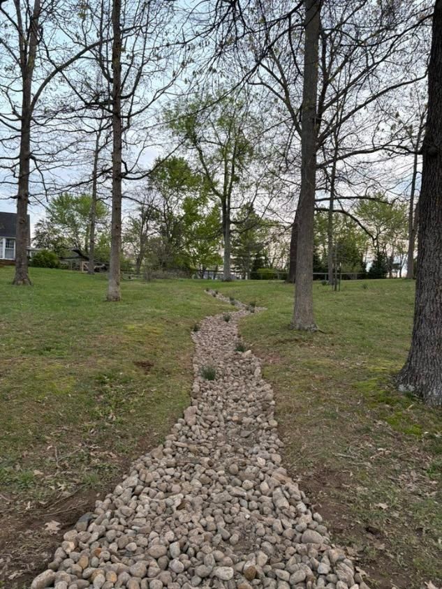 Rock-lined drainage path through a grassy park with leafless trees under a cloudy sky