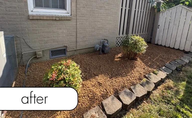 Landscaped side yard with mulch, small shrubs, and stone edging beside a house.