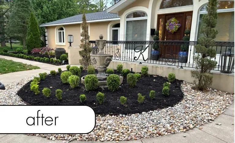Front yard landscaping with stone fountain, black mulch, and trimmed shrubs beside a house entrance.