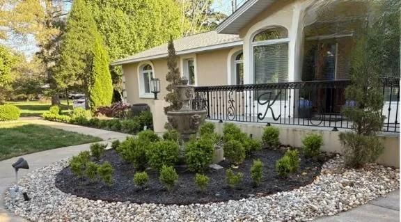 Front yard landscaping with shrubs and stone mulch beside a house and front porch