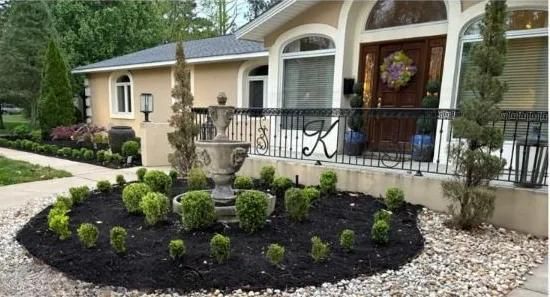 Front entrance of a house with arched windows, black railing, and a circular flower bed with a decorative urn.