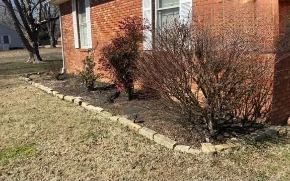 Brick house with a narrow stone border and leafless shrubs along the foundation.