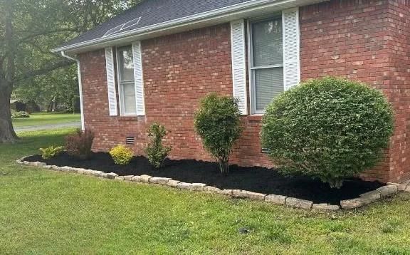 Brick house front with white shutters, small shrubs, and fresh black mulch along the foundation
