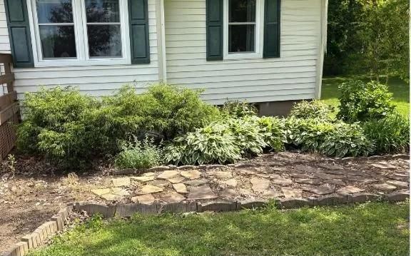 House front with green shrubs and a stone border in a grassy yard