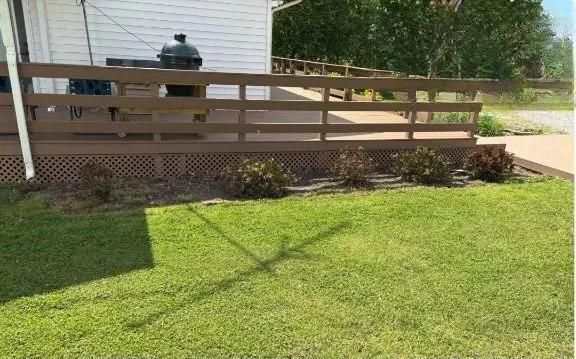 Wooden deck ramp beside a house, with a grill on the patio and a green lawn in front.