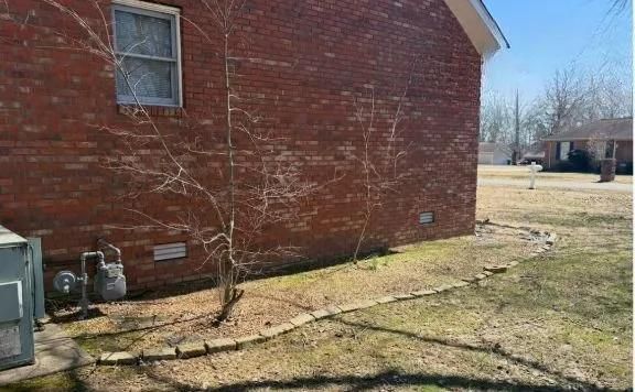 Brick house side yard with sparse grass, a small tree, and utility boxes near the wall