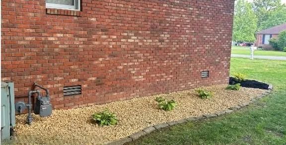 Mulched flower bed along a brick house with small plants and a grassy yard