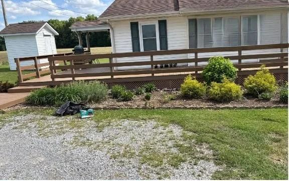 House with wooden deck, landscaped flower bed, and gravel driveway in the foreground