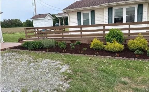 Front yard with wooden ramp railing, mulched flower bed, and beige house exterior