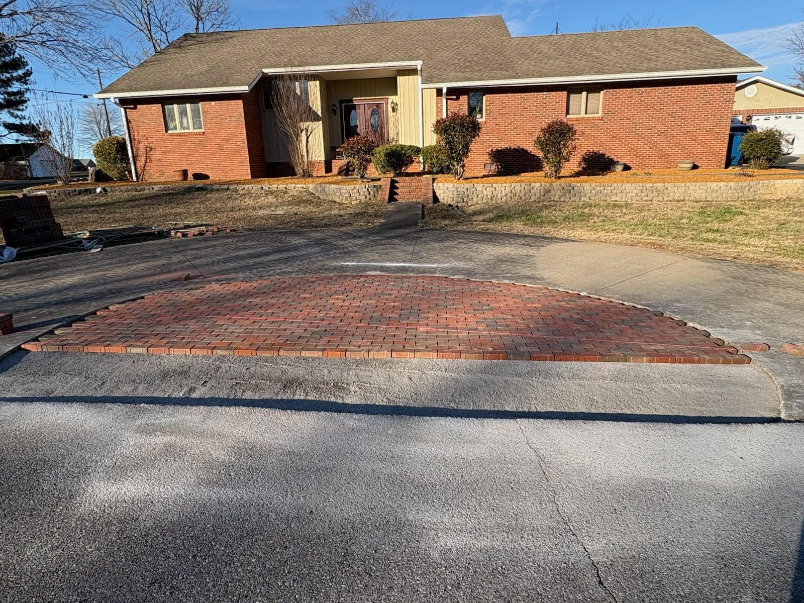 Brick house with front driveway and walkway, bordered by a low stone wall and winter grass.