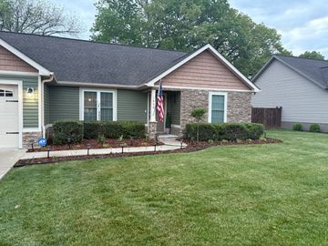 Brick house exterior with white shutters, trimmed shrubs, and fresh black mulch along the foundation