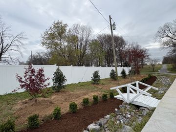 Front yard landscaping with trimmed shrubs, fresh mulch, green lawn, and a concrete walkway beside a house