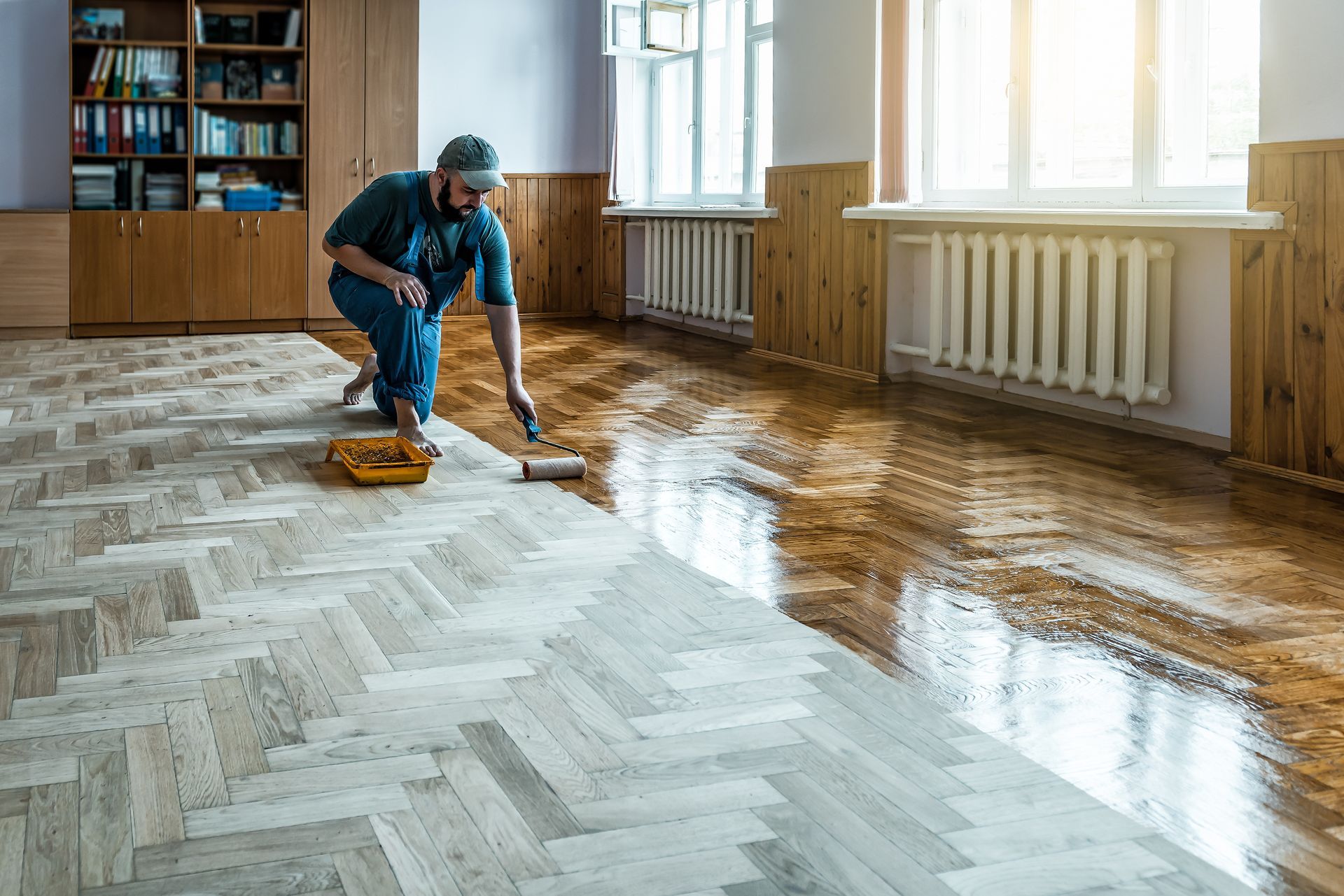 Worker using a roller to apply coating to hardwood floor.