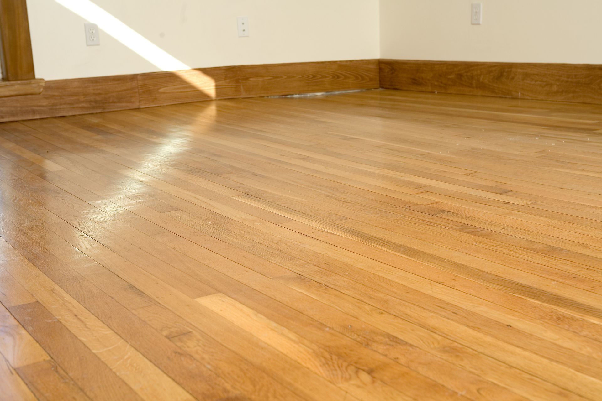 Polished light oak hardwood floor with wood baseboards in empty room with natural sunlight.