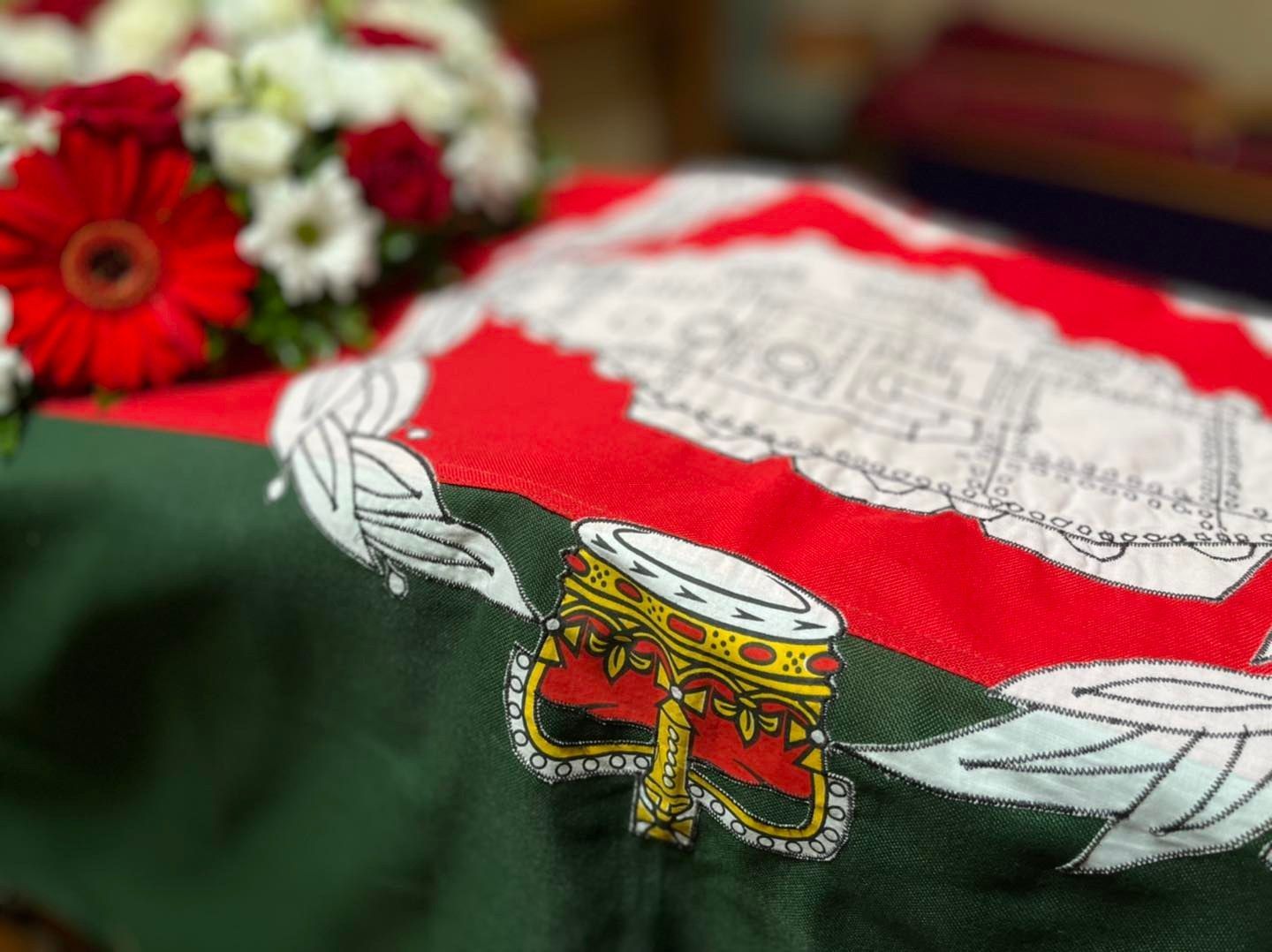 A coffin is laying on a table with flowers in the background.