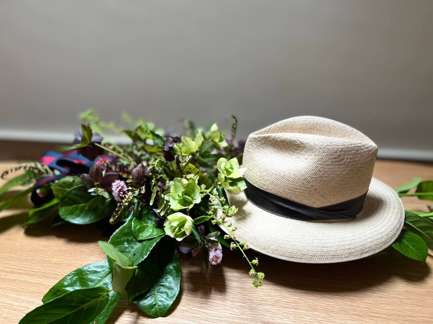 A hat is sitting on top of a wooden table next to a bouquet of flowers.