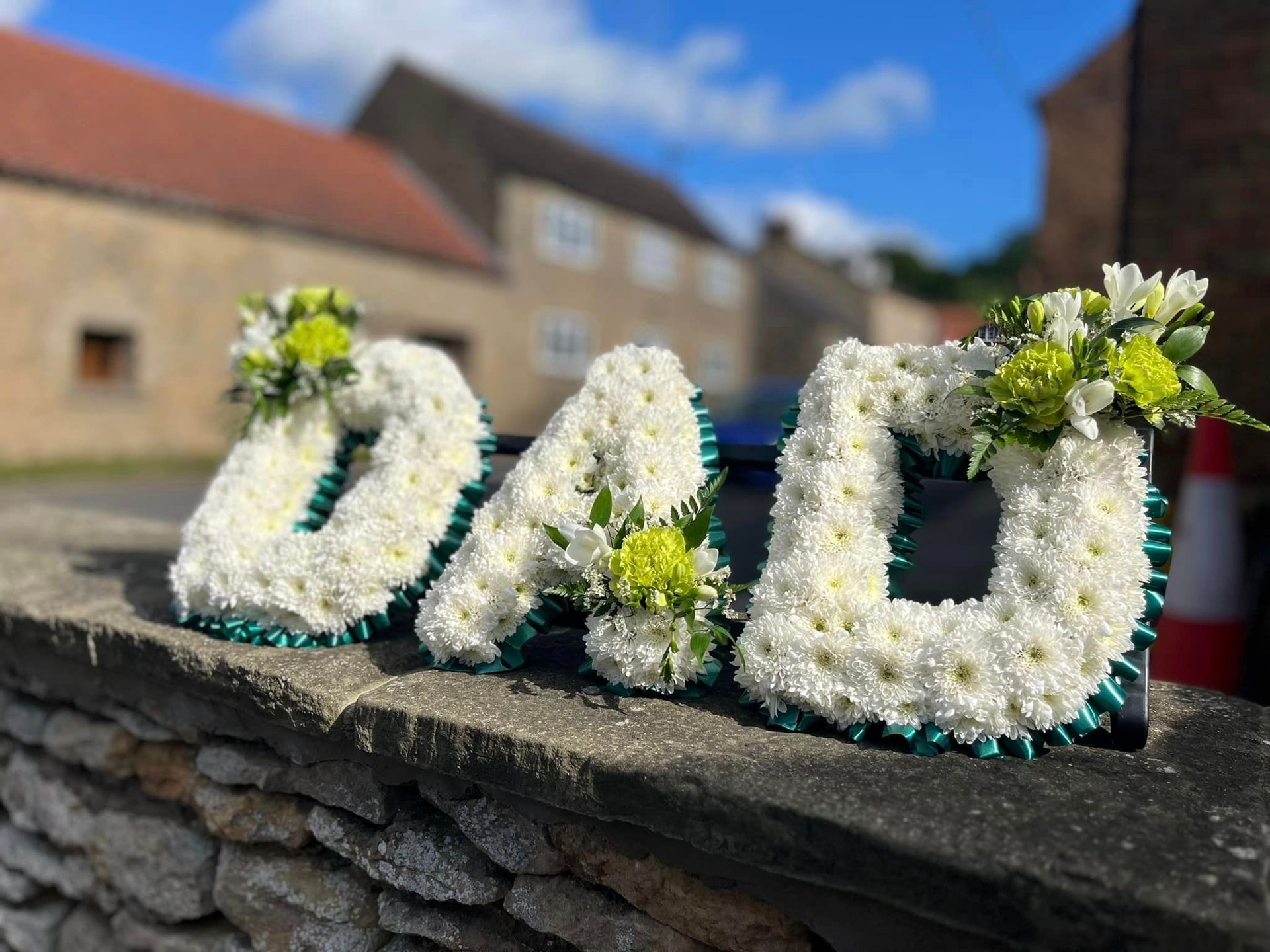 The word dad is made of white flowers on a stone wall.