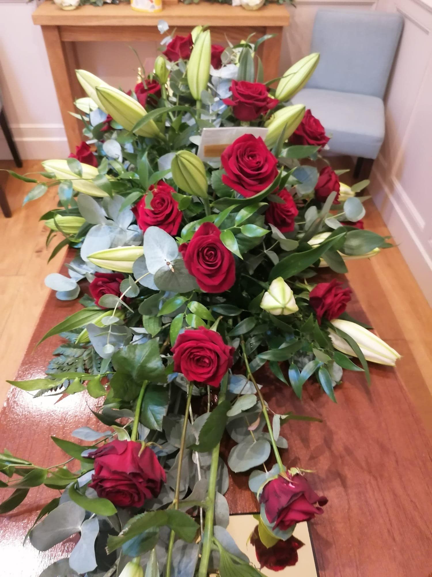 A wooden table topped with red roses and lilies.