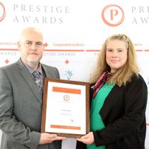 A man and a woman are holding a framed certificate for the prestige awards