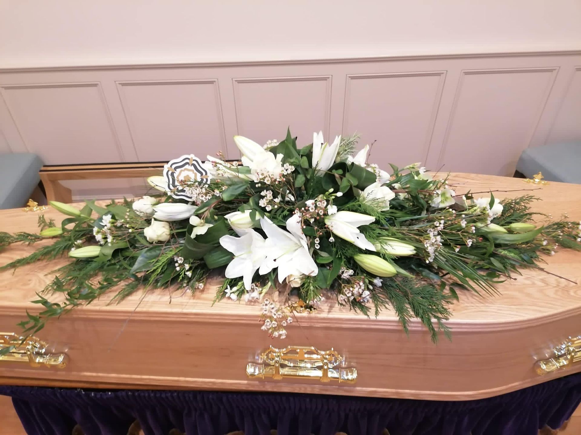 A coffin is decorated with white flowers and greenery.