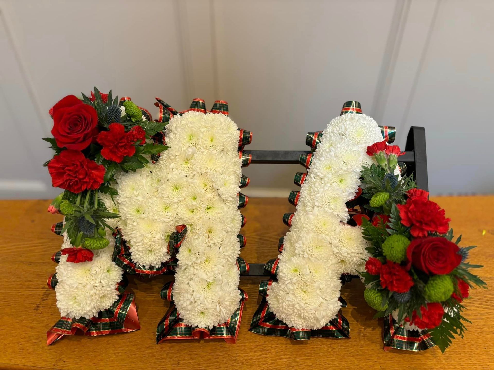 The letter m is made of flowers and is sitting on a wooden table.