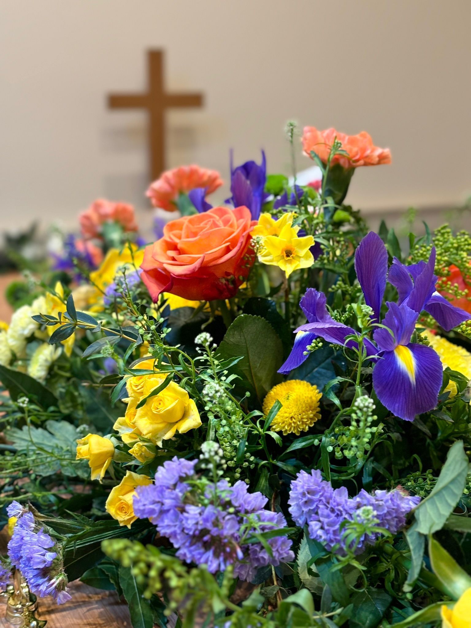A bunch of flowers are sitting on a table with a cross in the background.