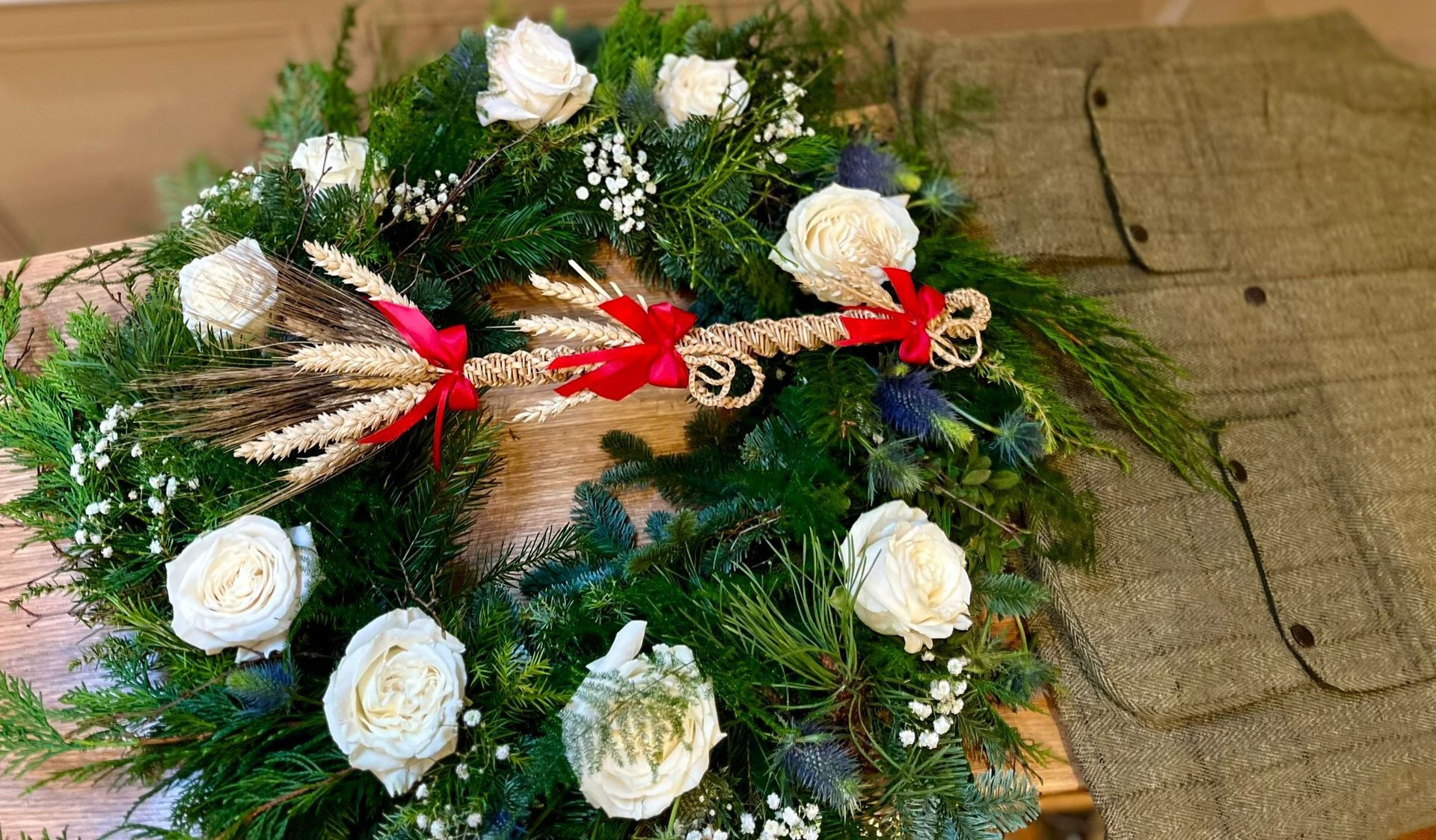 A wreath with white flowers and greenery is sitting on top of a wooden table.