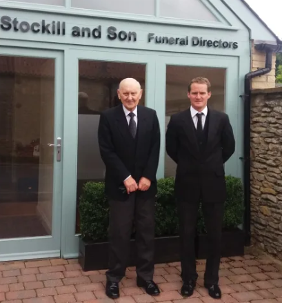 Two men standing in front of a building that says stockill and son funeral directors