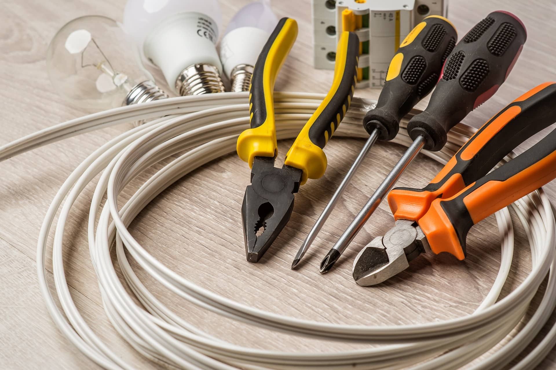 Coiled white cables with yellow, black, and orange pliers and screwdrivers on a light wooden surface
