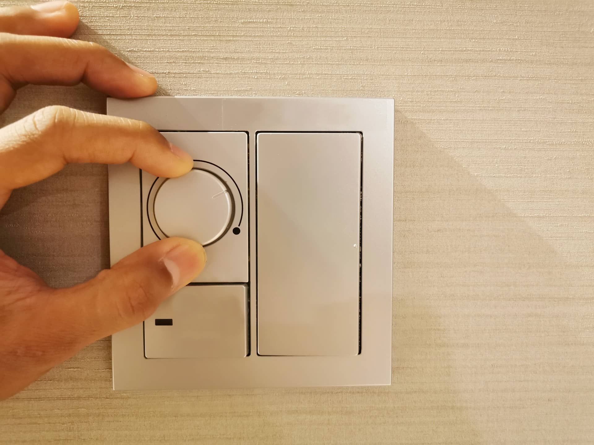 Hand adjusting a wall dimmer switch next to a blank light switch on a beige wall