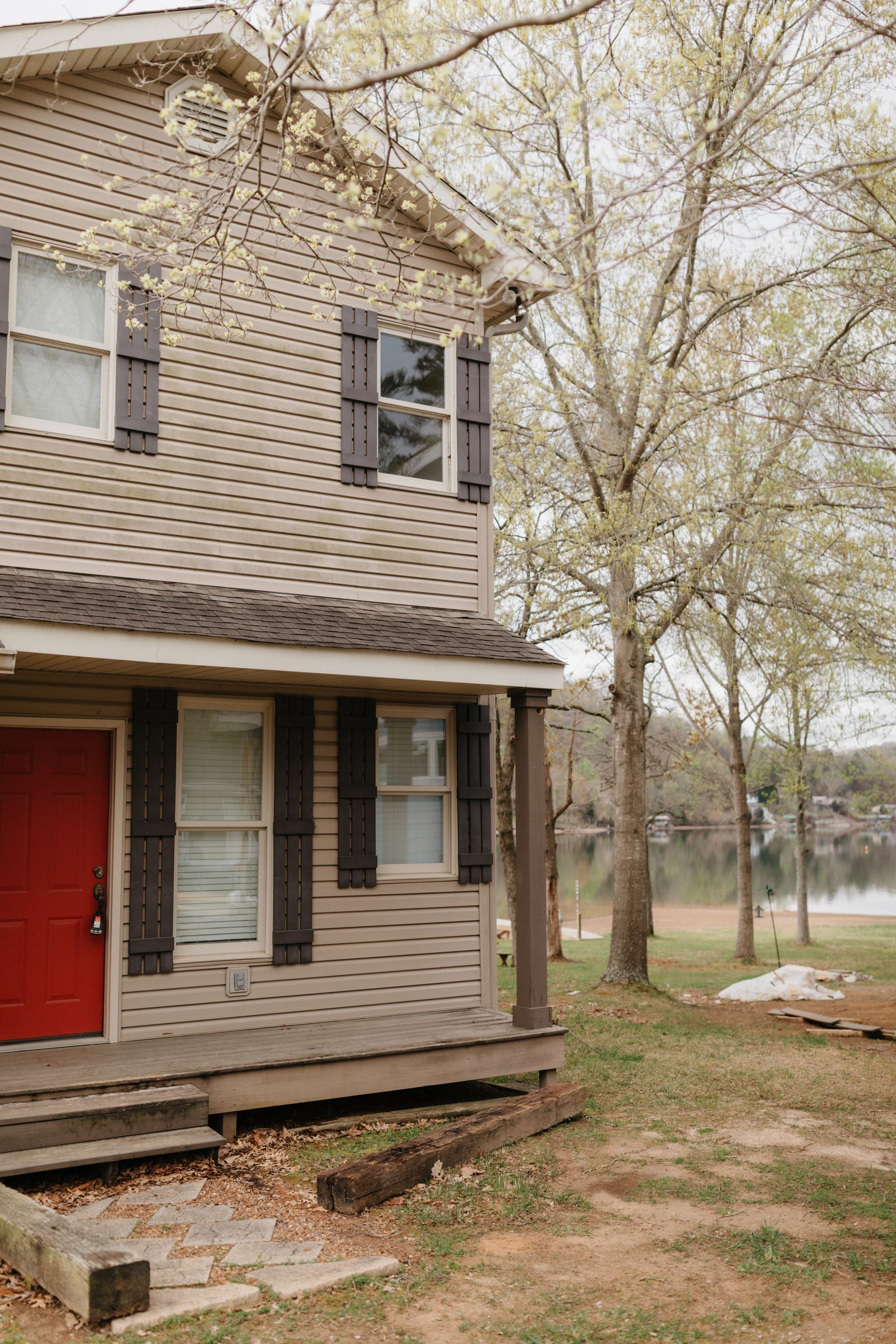 A house with a red door and black shutters is sitting next to a lake.