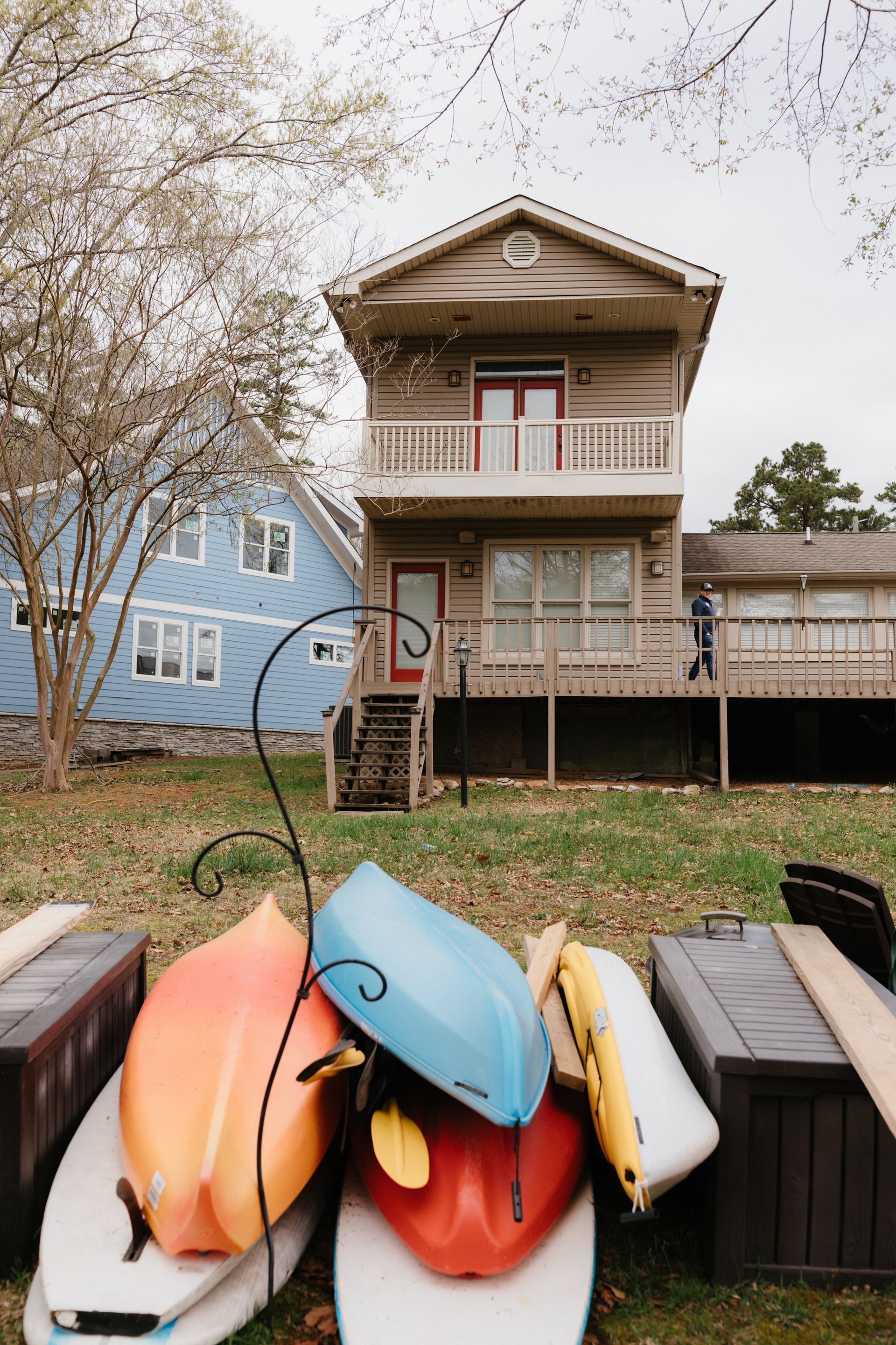 A bunch of kayaks are stacked on top of each other in front of a house.
