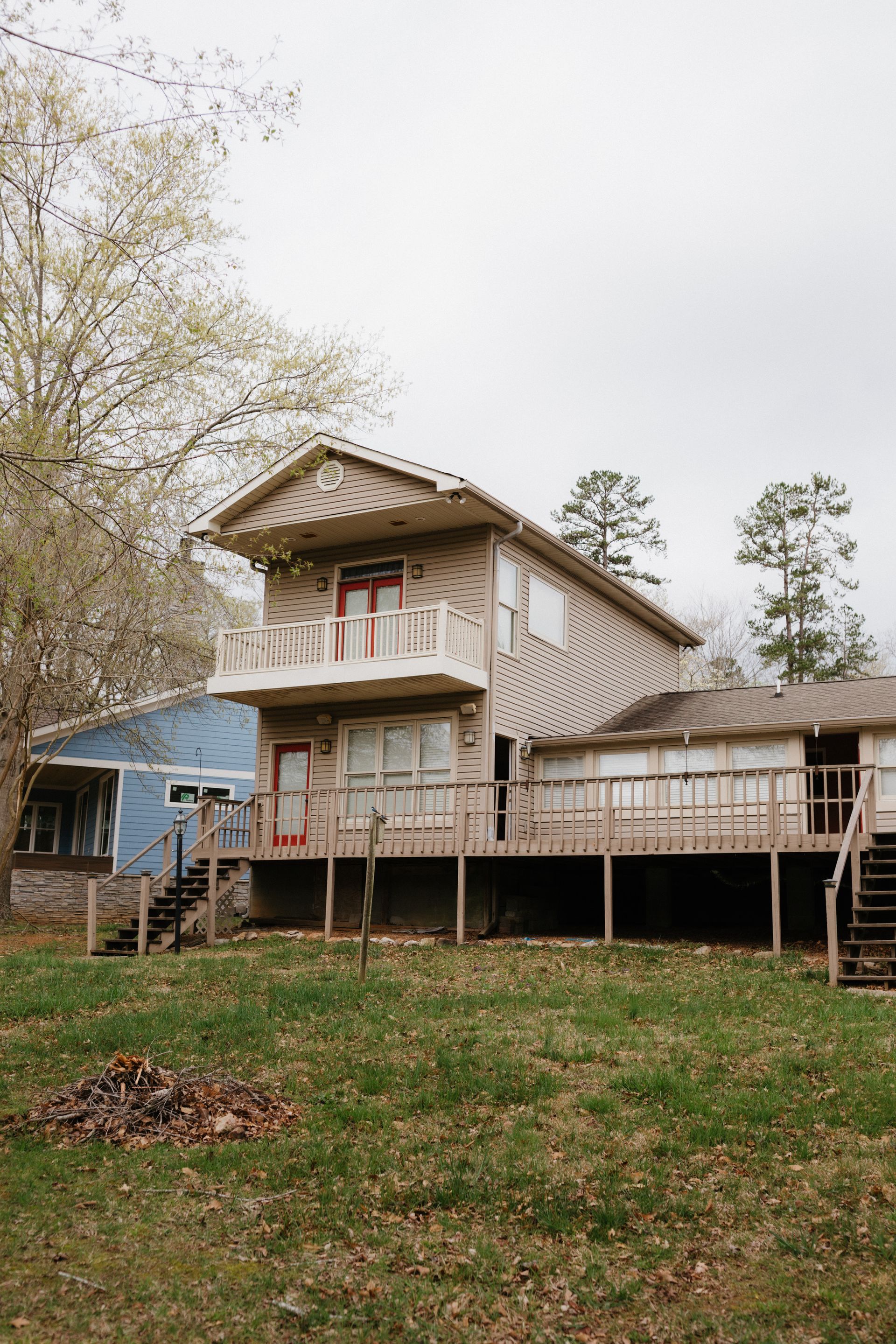A house with a large deck and stairs is sitting on top of a lush green field.