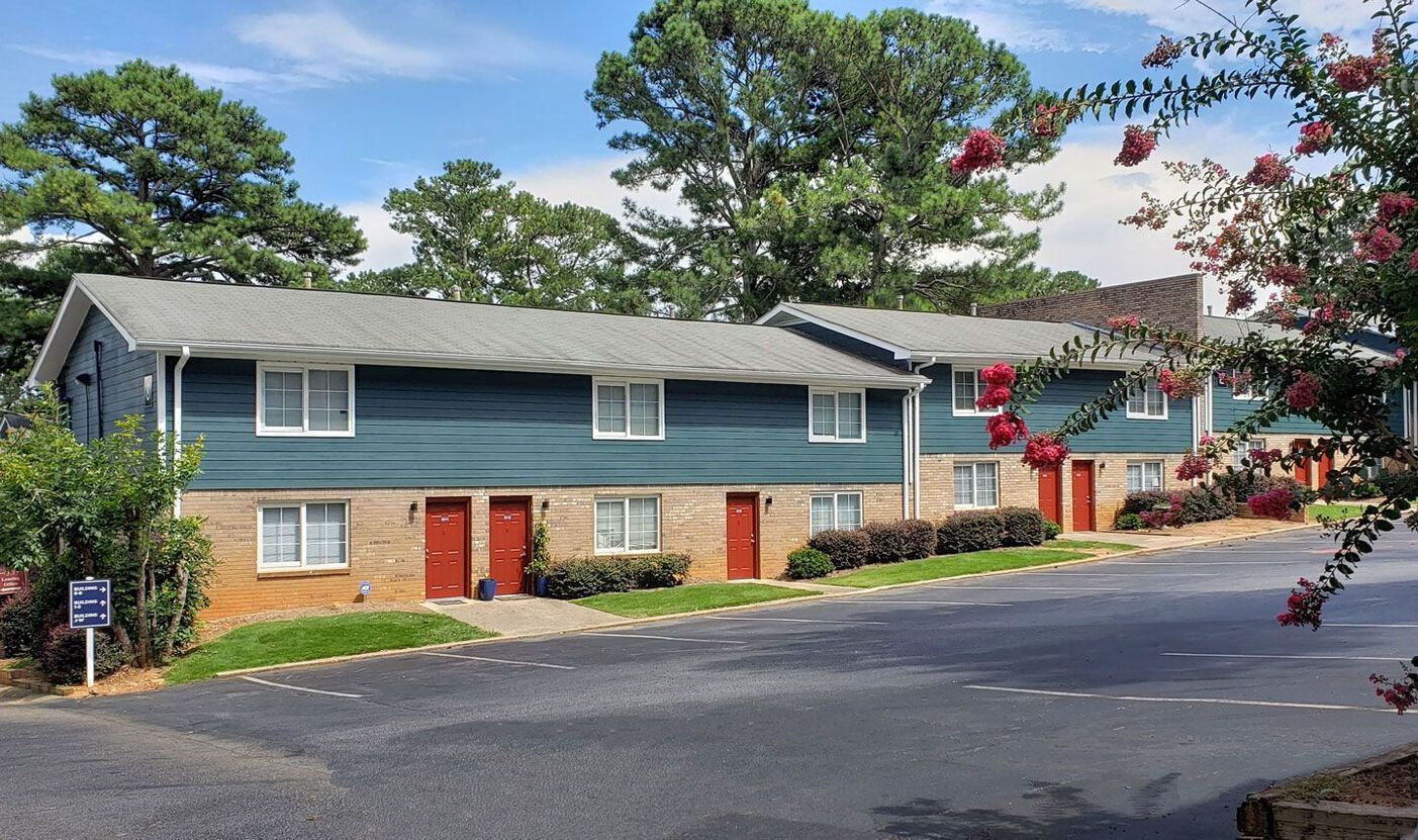 Two-story apartment buildings with blue siding and red doors; set in a residential area with trees and a driveway.