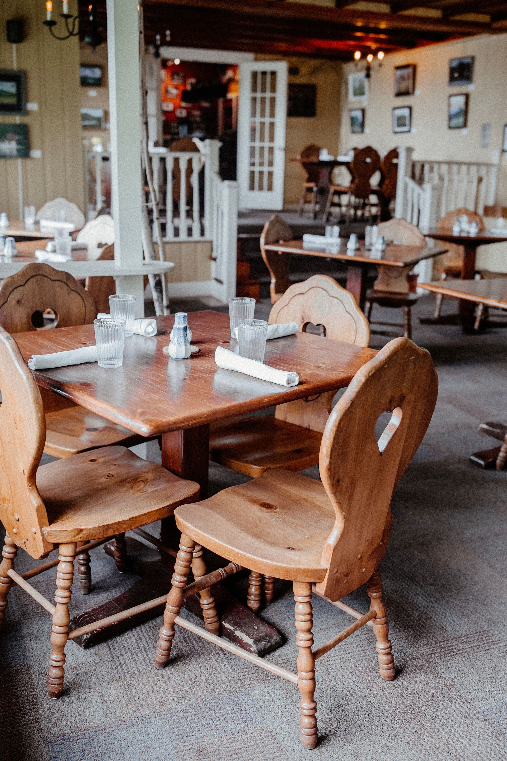 Rustic restaurant dining room with wooden chairs and tables, white walls, and framed art on the walls