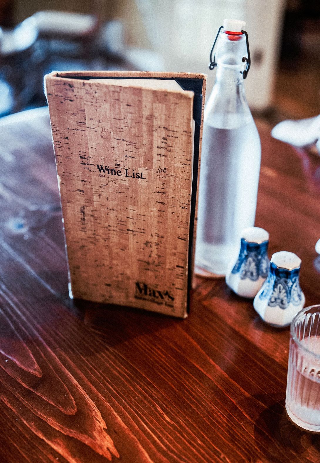 Vintage menu beside silver bottle and small white condiment shakers on a wooden table