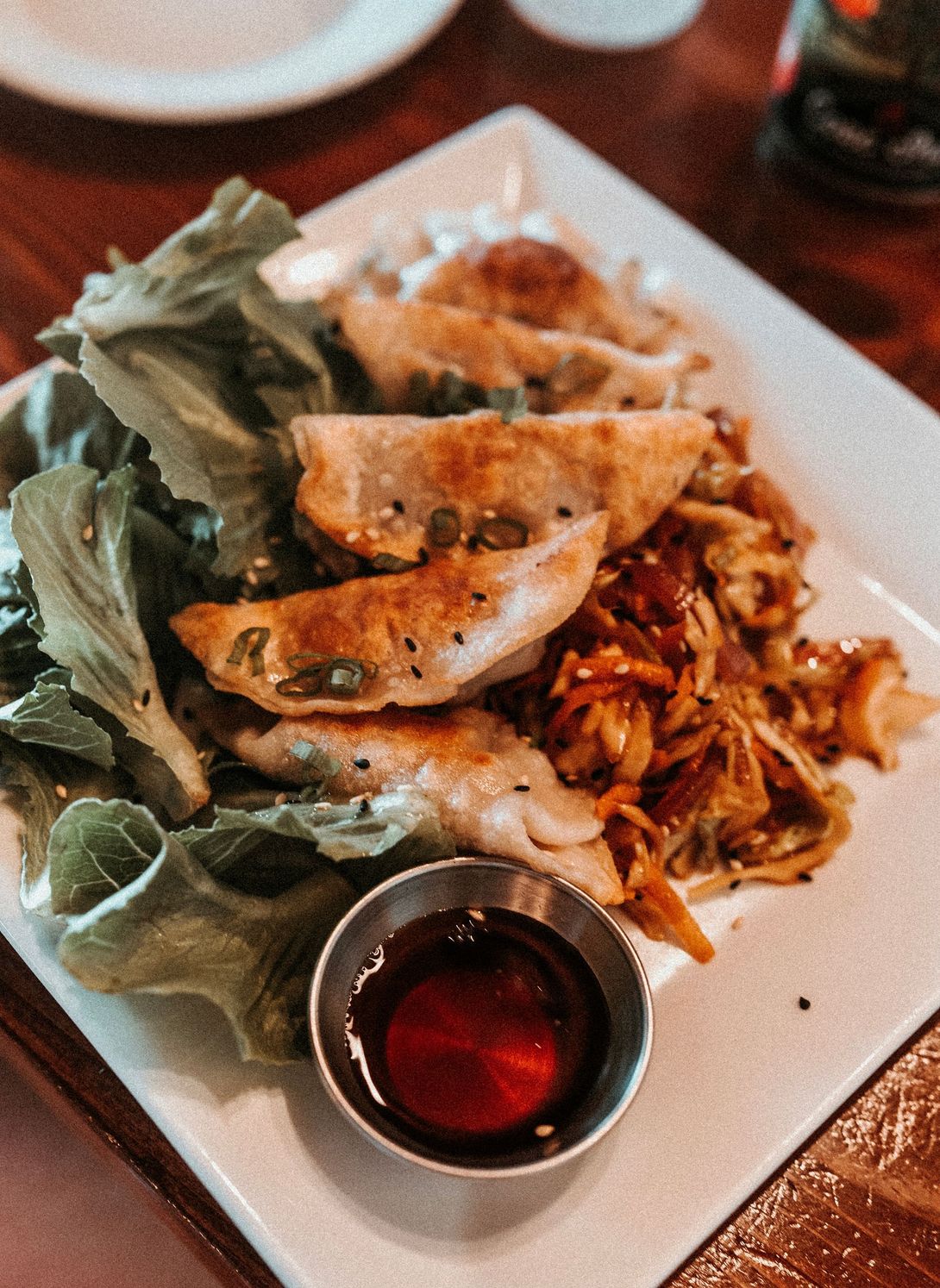 Plated dumplings with greens and dipping sauce on a white rectangular dish
