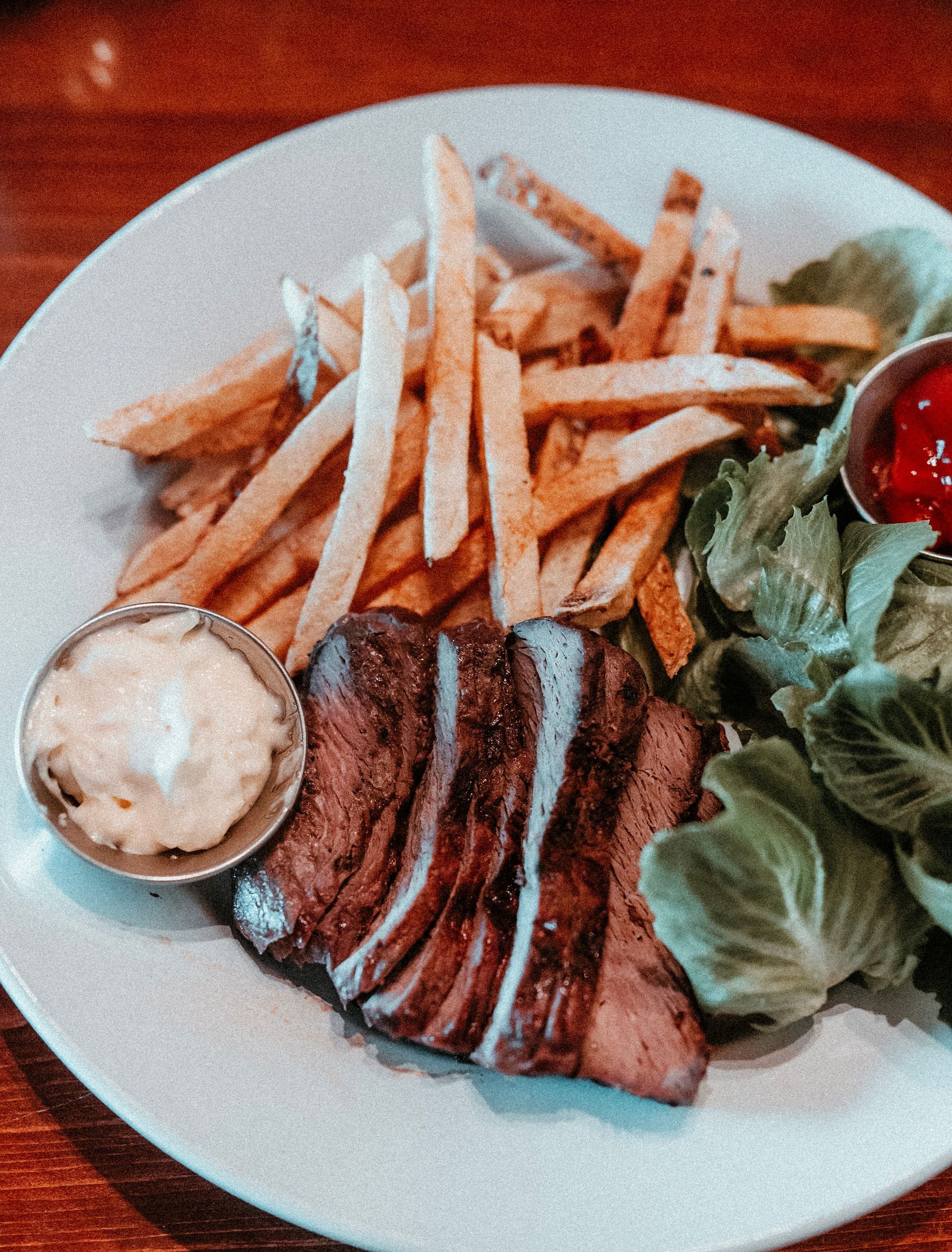 Grilled steak with fries, salad, and a small cup of sauce on a white plate