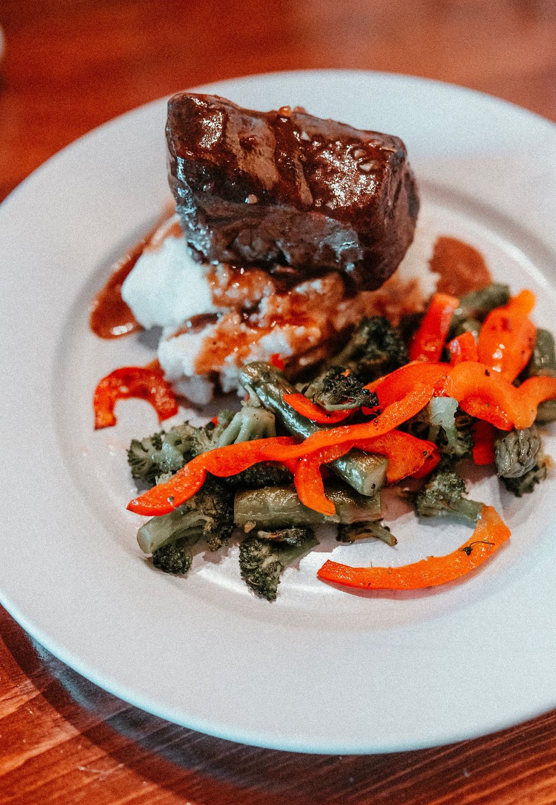 Plated meat entrée with greens and red peppers on a white dish, garnished with sauce