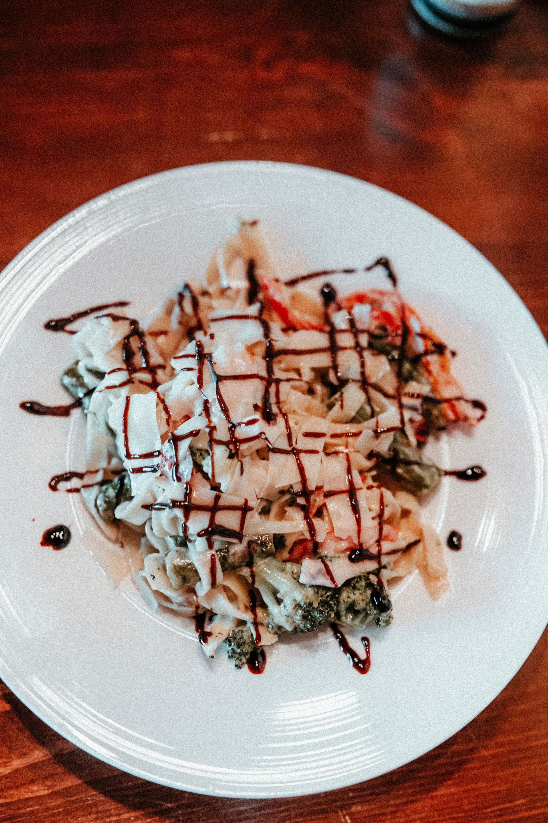 Dessert on a white plate, drizzled with chocolate and caramel sauces on a wooden table.