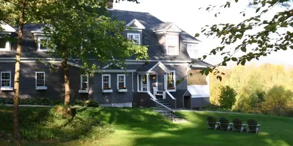 Large gray house with white trim beside a green lawn and trees in daylight