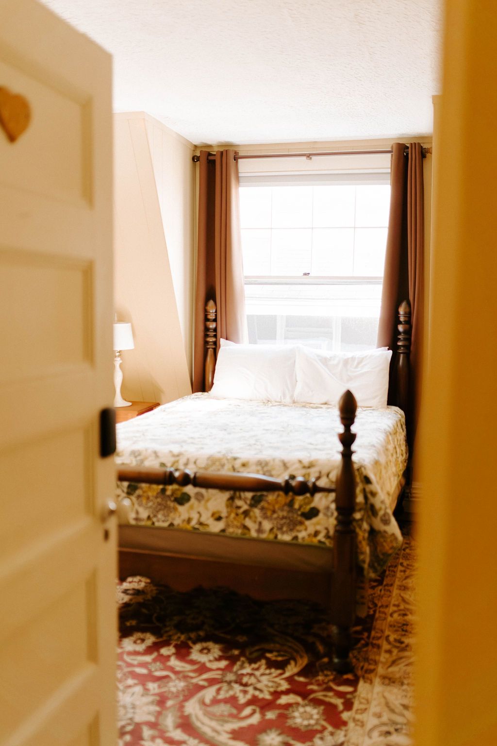 Cozy bedroom with a wooden bed, white bedding, brown curtains, and a window in soft light