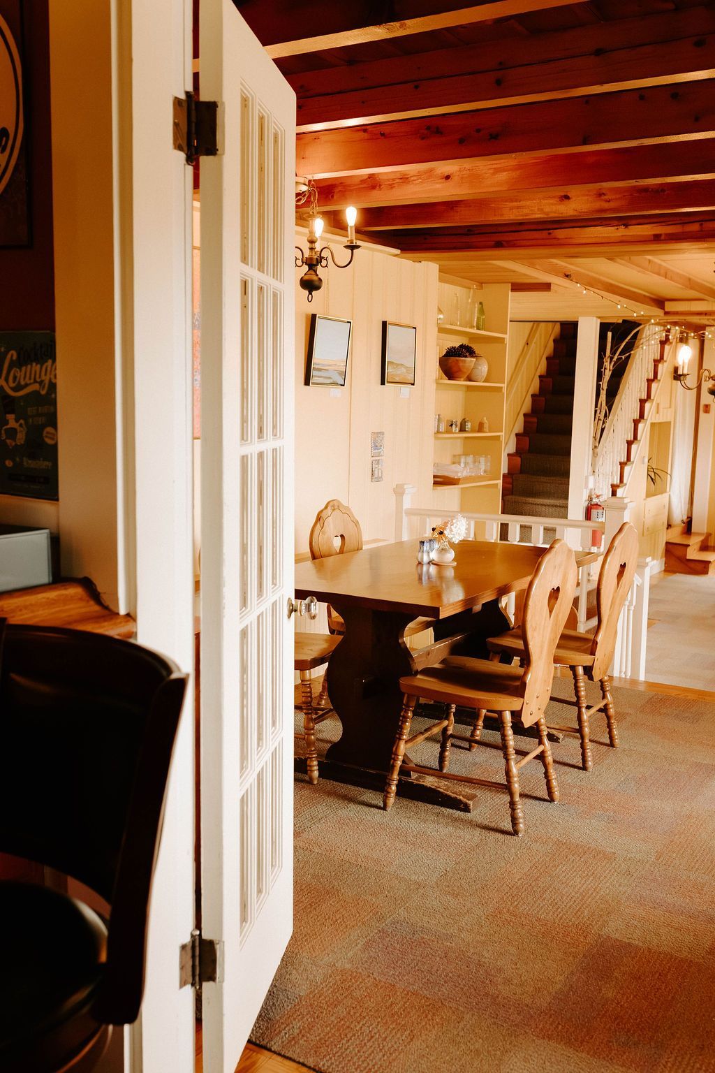 Cozy rustic dining room with wood beams, dining table, chairs, and staircase in the background